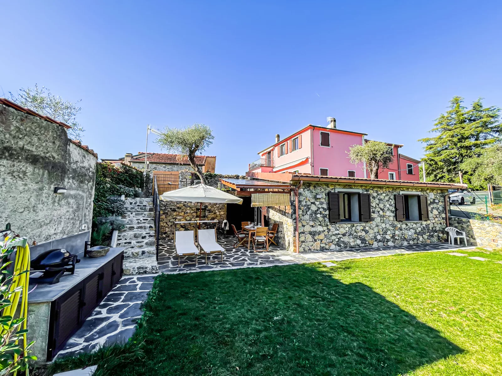 I Particolari vista dal giardino, con il barbecue, l'ombrellone e la casa rosa sullo sfondo