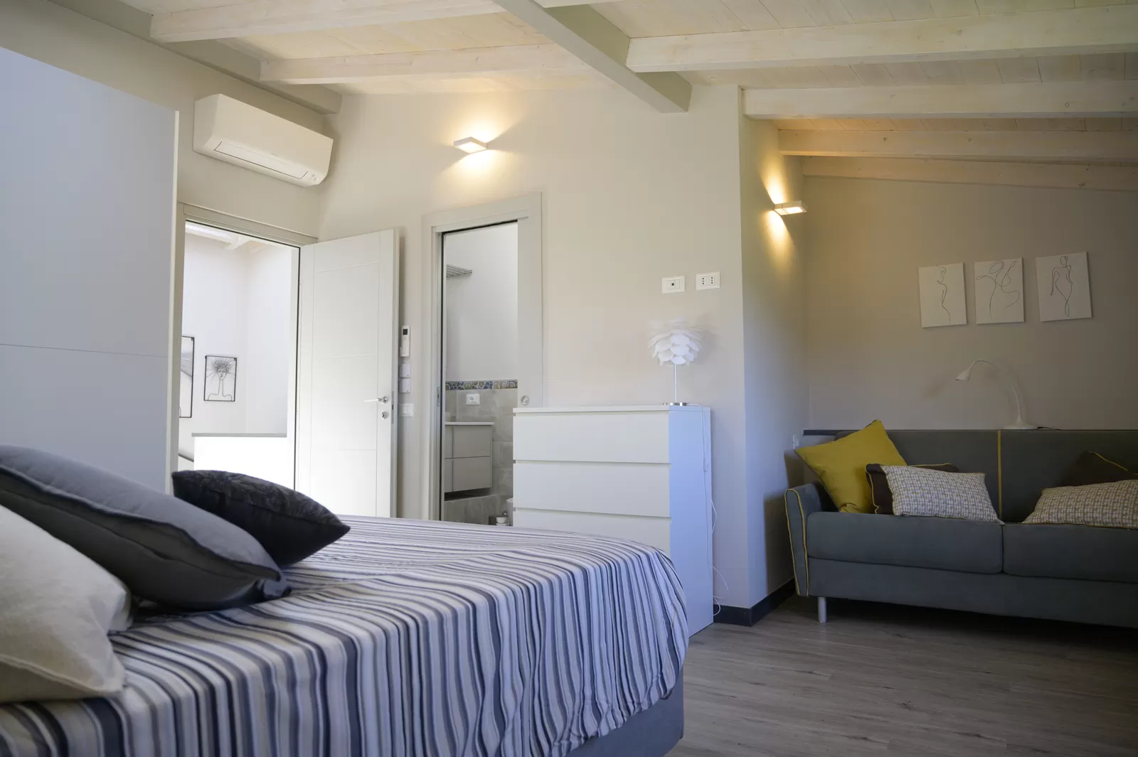 Una camera al secondo piano di Ritratto di Donna, con il divano letto grigio accanto al letto matrimoniale e la porta del bagno